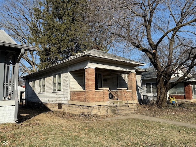 view of side of home featuring covered porch, brick siding, and a lawn