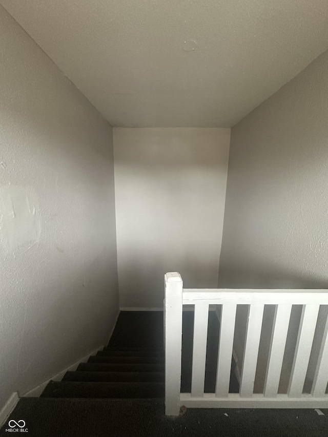 staircase featuring a textured wall and carpet floors