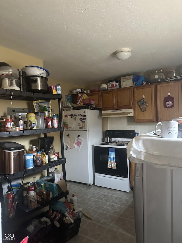 kitchen with electric stove, under cabinet range hood, a textured ceiling, freestanding refrigerator, and brown cabinetry