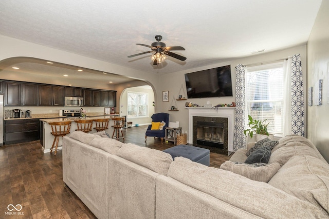 living room featuring recessed lighting, arched walkways, a premium fireplace, ceiling fan, and dark wood-style flooring