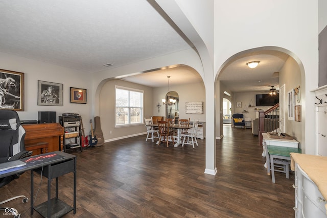 dining room with dark wood-type flooring, baseboards, stairs, ceiling fan with notable chandelier, and arched walkways