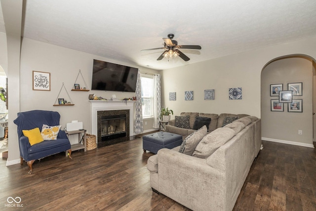 living room with dark wood-type flooring, arched walkways, a high end fireplace, and ceiling fan