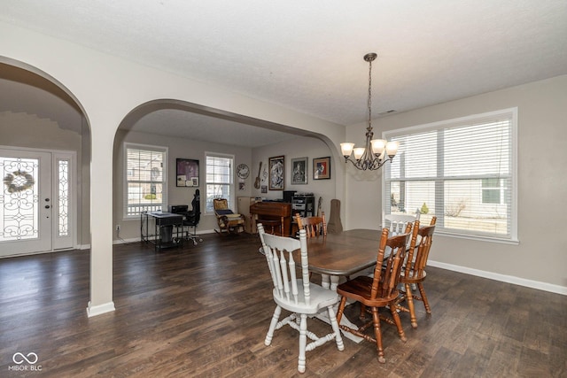 dining space with a chandelier, arched walkways, dark wood-type flooring, and baseboards