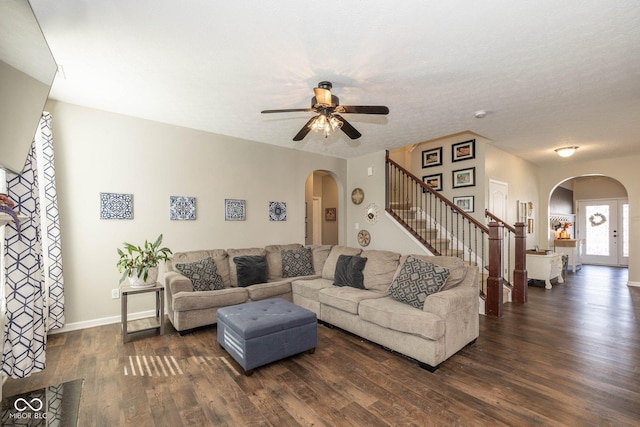 living area featuring a ceiling fan, dark wood finished floors, arched walkways, baseboards, and stairs