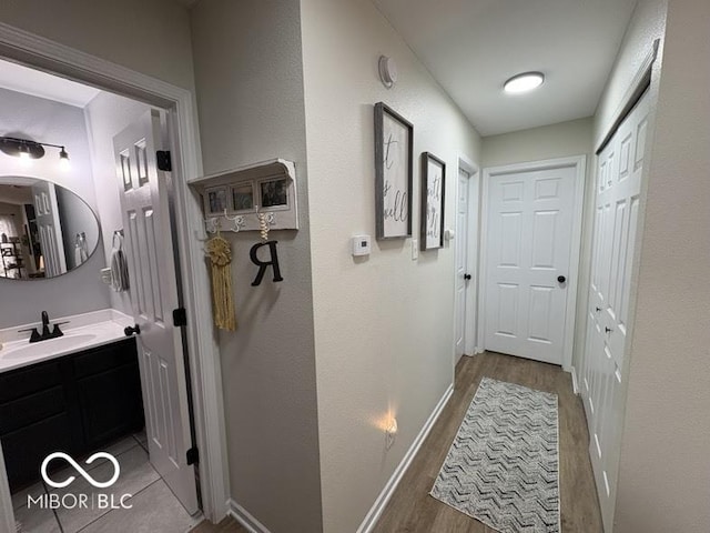 hallway featuring wood finished floors, baseboards, and a sink