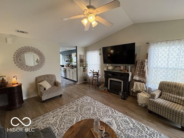 living area featuring a ceiling fan, wood finished floors, visible vents, lofted ceiling, and a fireplace