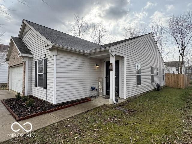 view of side of property featuring fence, driveway, roof with shingles, a garage, and a lawn