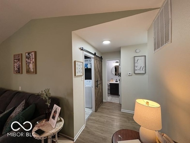 hall featuring wood finished floors, visible vents, baseboards, lofted ceiling, and a barn door