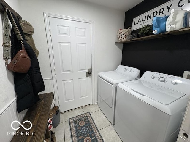 laundry area with light tile patterned floors, laundry area, washing machine and dryer, and a wainscoted wall