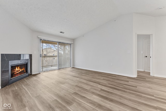 unfurnished living room featuring light wood finished floors, baseboards, vaulted ceiling, a fireplace, and a textured ceiling