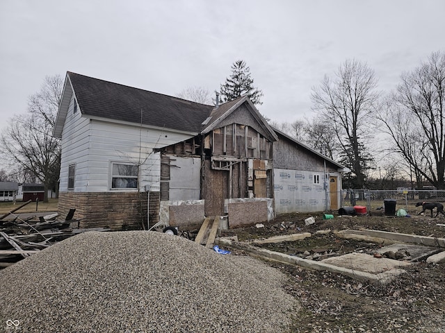 view of front of home with fence, stone siding, and a shingled roof