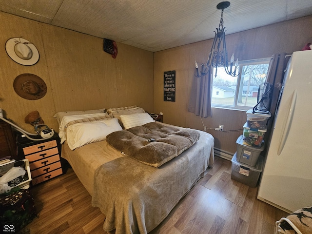 bedroom featuring wood finished floors, freestanding refrigerator, wood walls, a notable chandelier, and baseboard heating