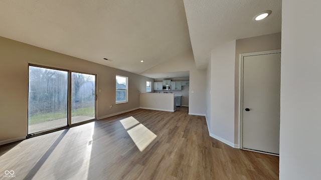 unfurnished living room featuring baseboards, light wood-style floors, and vaulted ceiling