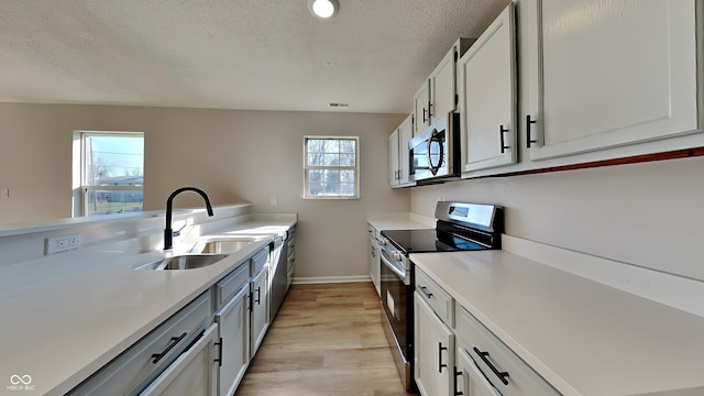 kitchen with light wood finished floors, light countertops, appliances with stainless steel finishes, a textured ceiling, and a sink