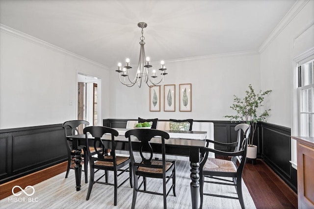 dining area with ornamental molding, wood finished floors, an inviting chandelier, wainscoting, and a decorative wall