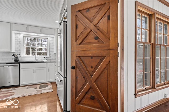 bar featuring light wood-style flooring, a sink, backsplash, a barn door, and dishwasher