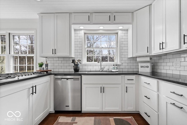 kitchen featuring dark countertops, decorative backsplash, appliances with stainless steel finishes, white cabinets, and a sink