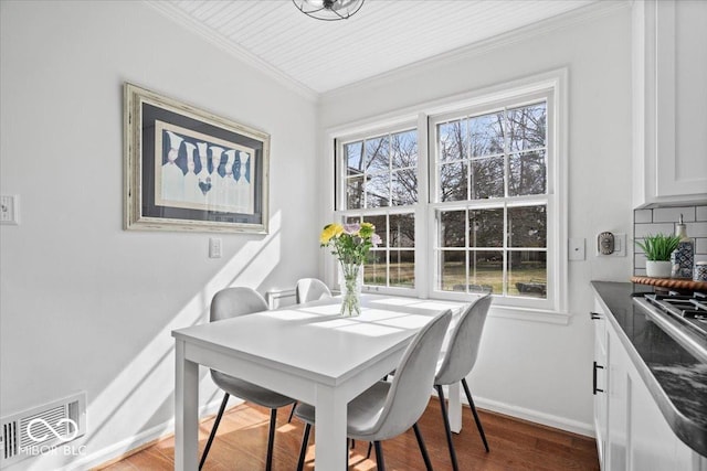 dining room featuring visible vents, ornamental molding, baseboards, and wood finished floors