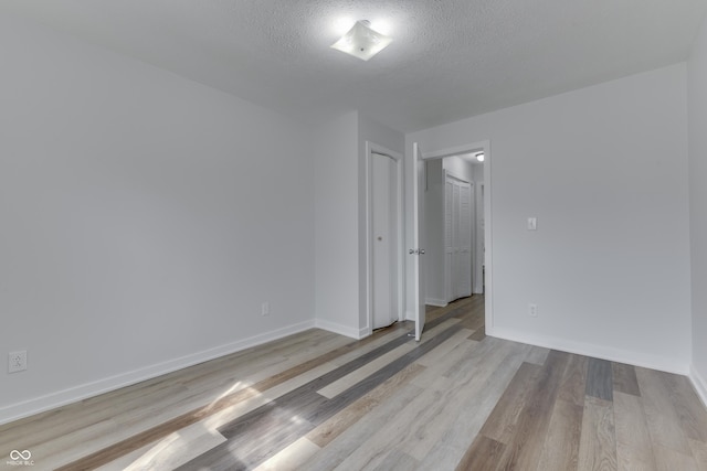 empty room featuring light wood-style floors, baseboards, and a textured ceiling