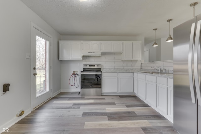 kitchen with a sink, light countertops, under cabinet range hood, appliances with stainless steel finishes, and tasteful backsplash