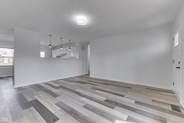 unfurnished living room with light wood-type flooring, visible vents, baseboards, and a textured ceiling