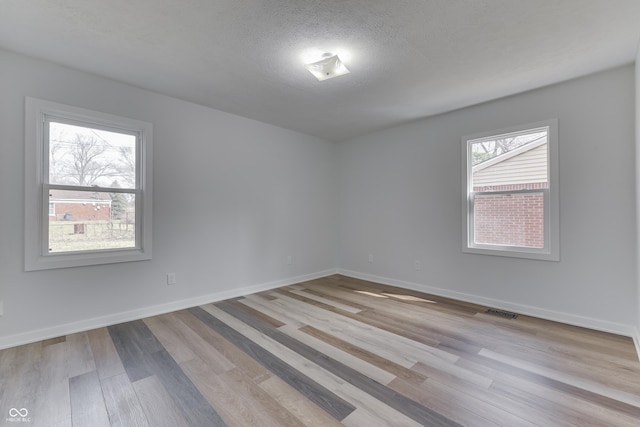 unfurnished room with a textured ceiling, baseboards, visible vents, and light wood-type flooring