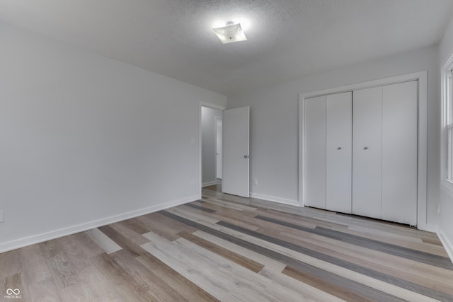 unfurnished bedroom with wood finished floors, baseboards, a closet, and a textured ceiling