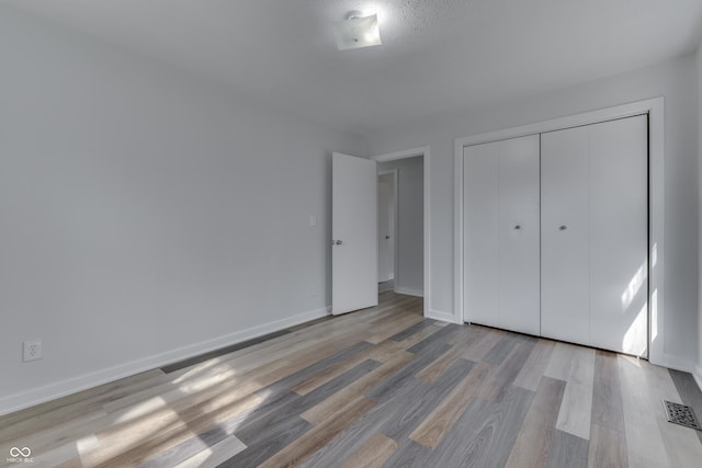 unfurnished bedroom featuring a closet, visible vents, baseboards, and light wood-style floors