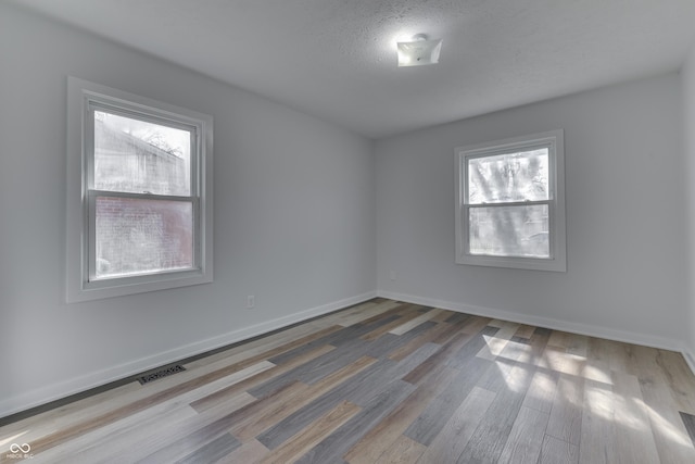 spare room featuring visible vents, baseboards, a textured ceiling, and wood finished floors