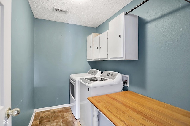 washroom featuring visible vents, washer and dryer, a textured ceiling, cabinet space, and baseboards