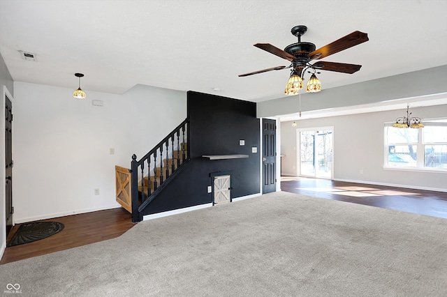 unfurnished living room with visible vents, ceiling fan with notable chandelier, carpet flooring, baseboards, and stairs