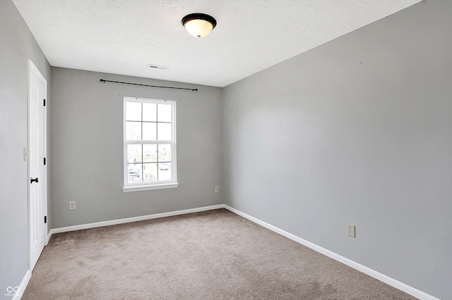 carpeted spare room with visible vents, baseboards, and a textured ceiling