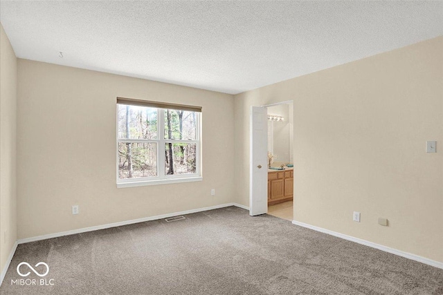 spare room with light carpet, visible vents, a textured ceiling, and baseboards