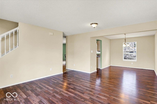 empty room with stairway, wood finished floors, baseboards, and a textured ceiling