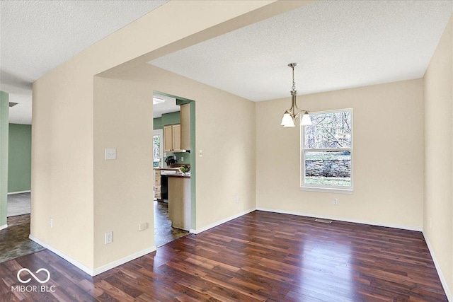 spare room featuring baseboards, a textured ceiling, an inviting chandelier, and wood finished floors