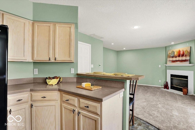 kitchen with carpet floors, a peninsula, light brown cabinetry, dark countertops, and open floor plan