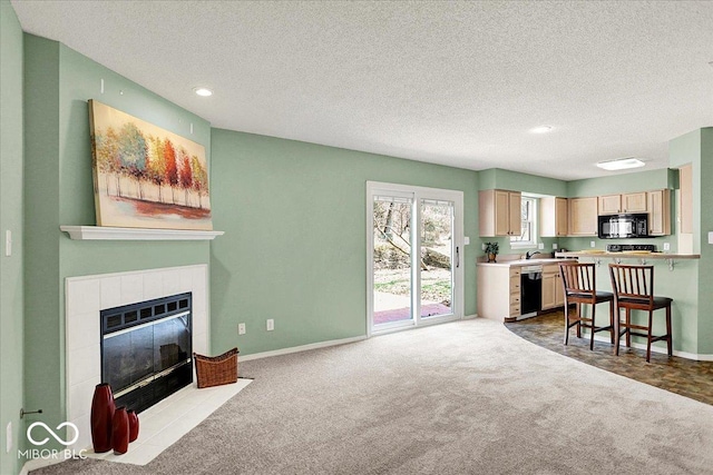 living room featuring dark carpet, a tile fireplace, a textured ceiling, and baseboards