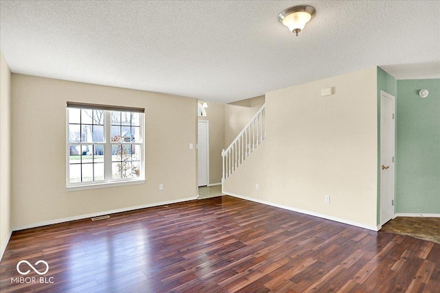 unfurnished living room with visible vents, a textured ceiling, wood finished floors, and stairs