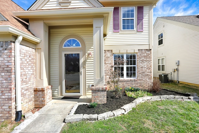 view of exterior entry with brick siding and central AC unit