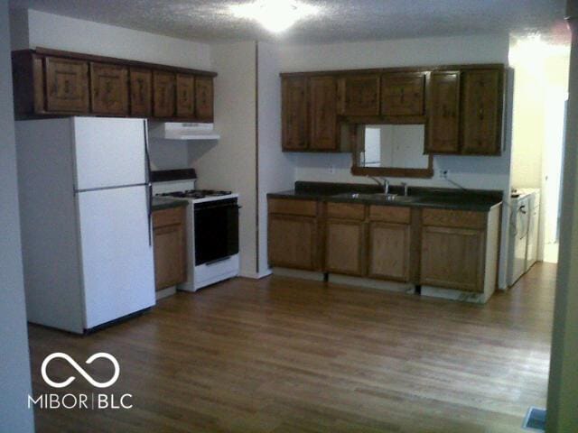 kitchen featuring a sink, dark countertops, wood finished floors, ventilation hood, and white appliances