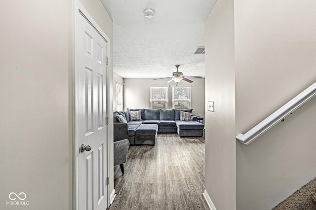 hall with visible vents, a textured ceiling, baseboards, and wood finished floors