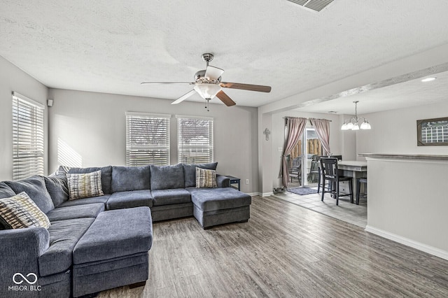 living area with ceiling fan with notable chandelier, wood finished floors, baseboards, and a wealth of natural light