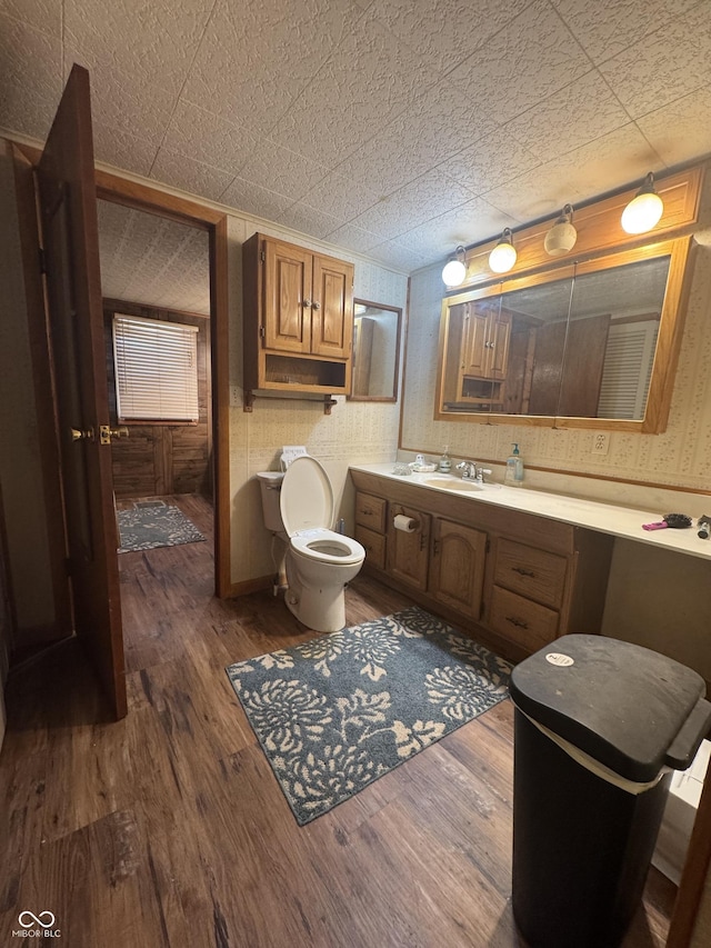bathroom with wallpapered walls, toilet, wood finished floors, an ornate ceiling, and vanity