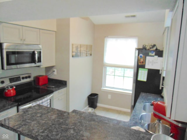 kitchen featuring dark stone countertops, a peninsula, appliances with stainless steel finishes, and white cabinets