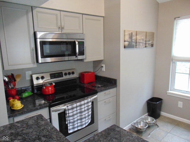 kitchen with dark stone countertops, baseboards, appliances with stainless steel finishes, and a healthy amount of sunlight