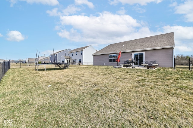 rear view of property featuring a yard, a trampoline, and a fenced backyard