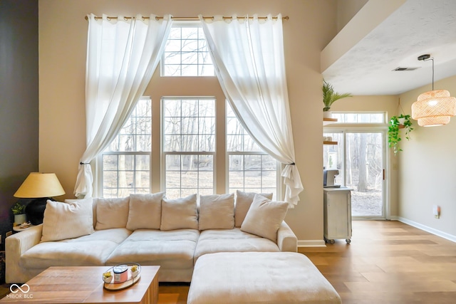 living area featuring a wealth of natural light, visible vents, baseboards, and wood finished floors