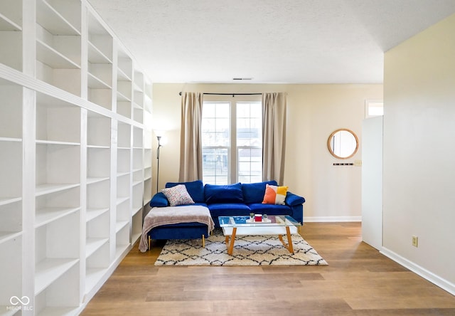 living area with visible vents, a textured ceiling, baseboards, and wood finished floors