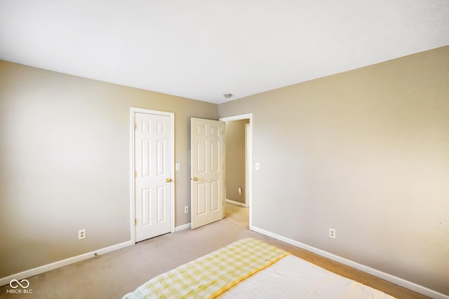 unfurnished bedroom with a closet, light colored carpet, and baseboards