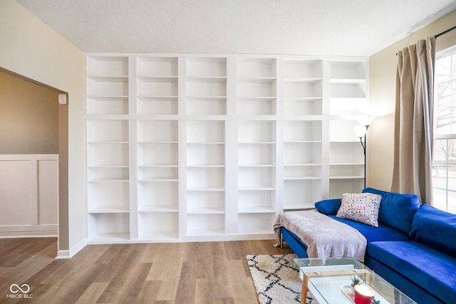 sitting room featuring built in shelves, wainscoting, wood finished floors, a decorative wall, and a textured ceiling